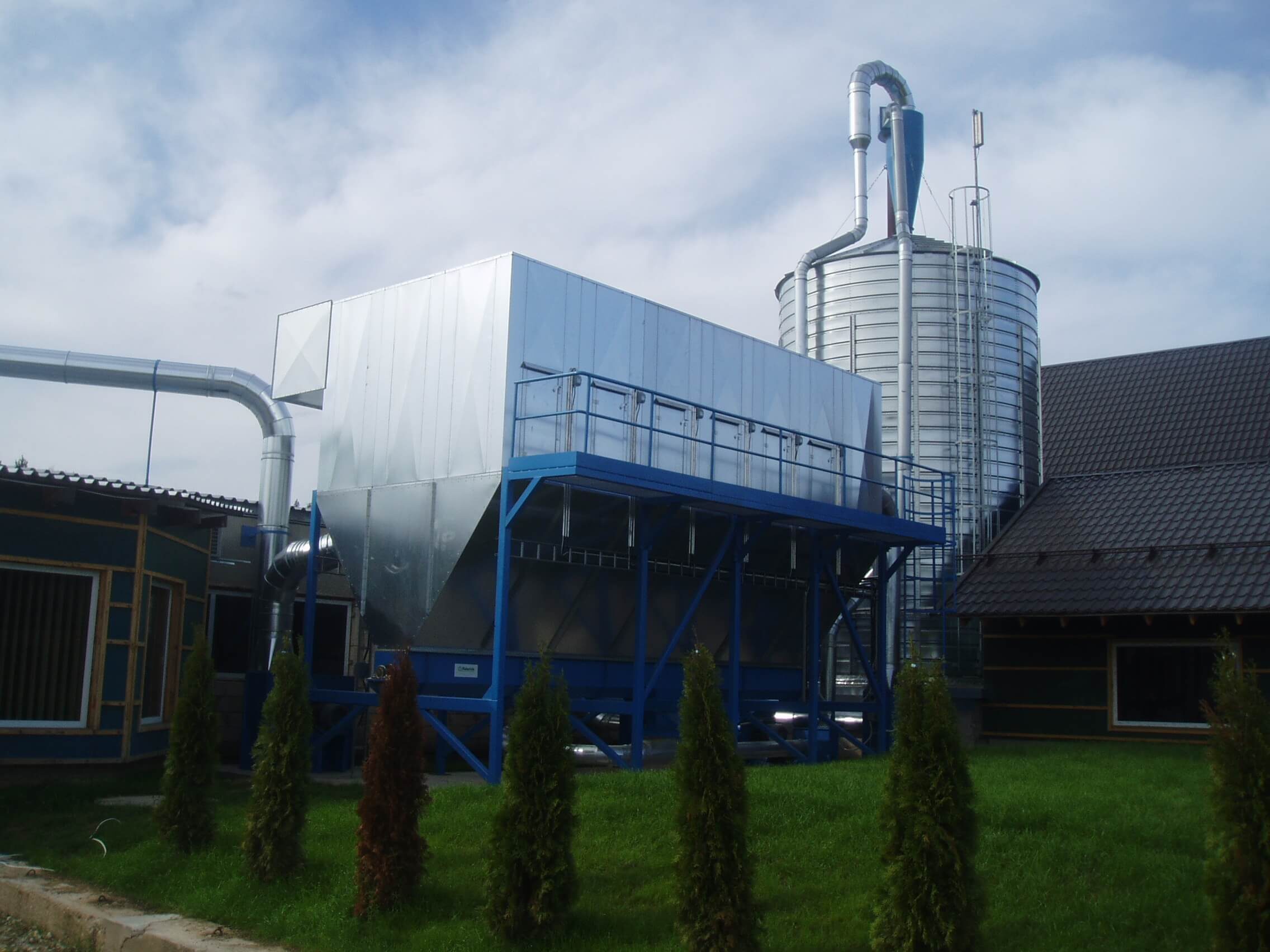Filtre d’aspiration sur châssis bleu et silo, devant un bâtiment de scierie