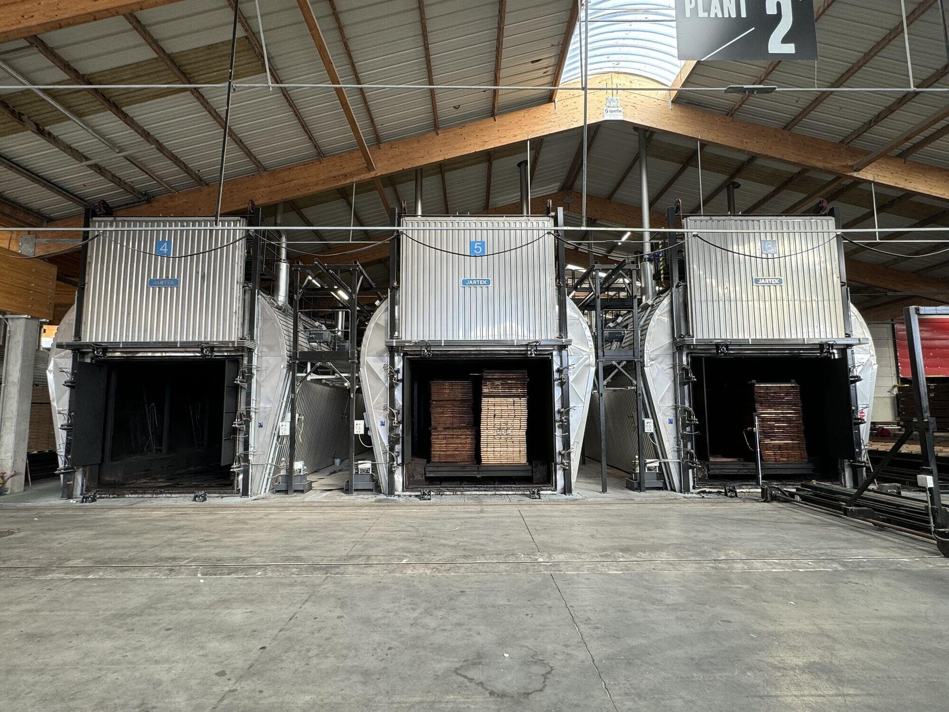 Trois fours de thermo-modification en inox, portes levées, deux chargés de bois traité