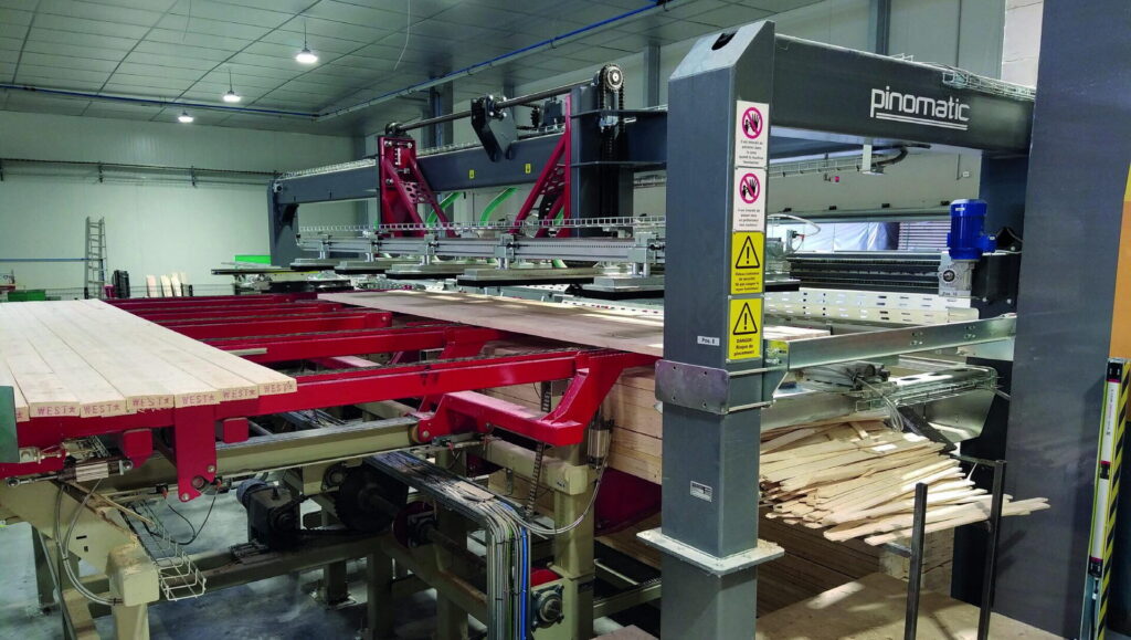 Empileur Pinomatic formant une couche de planches sur un convoyeur rouge