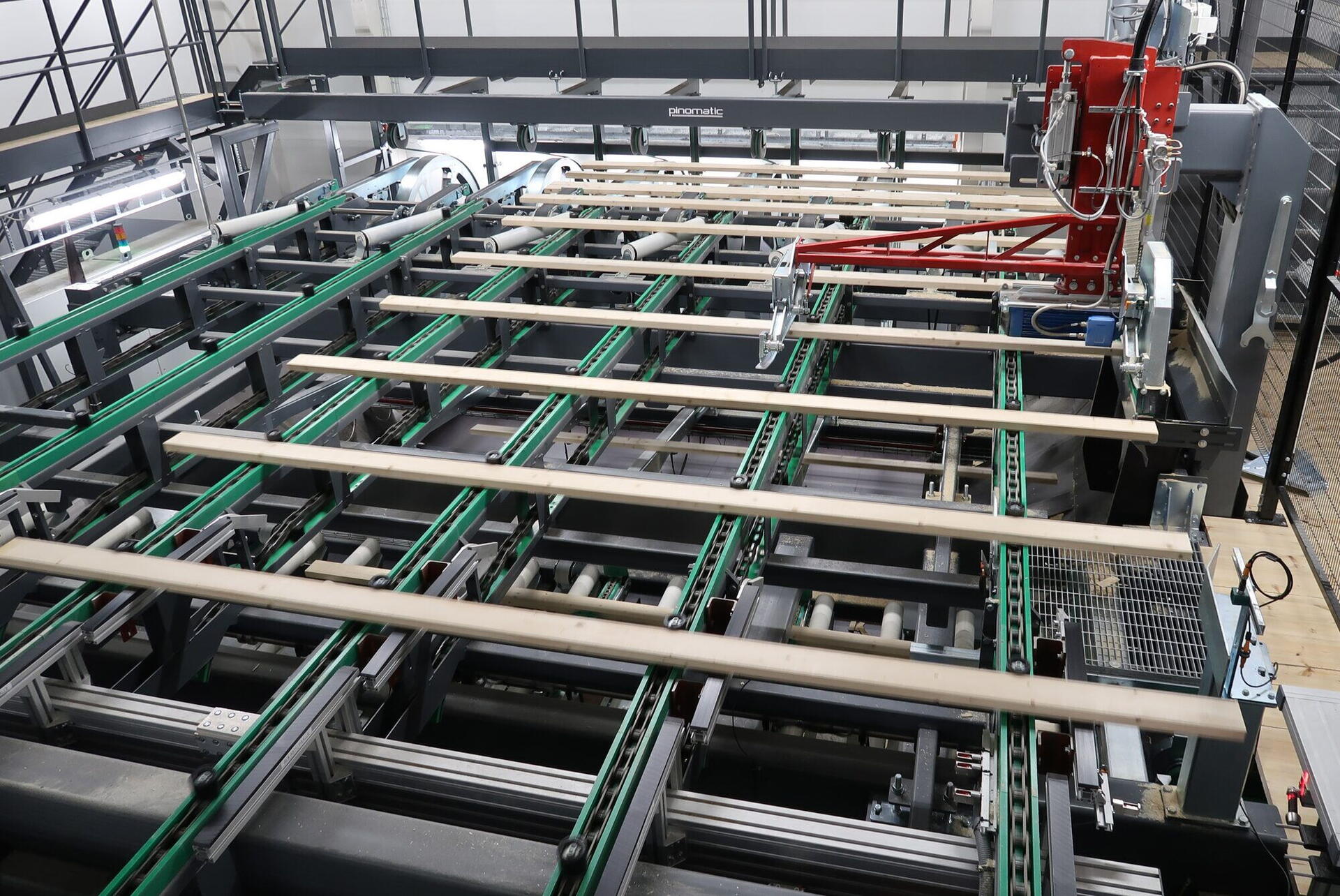 Table transversale à chaînes portant des planches espacées, bras d'alimentation rouge d'une ligne Pinomatic
